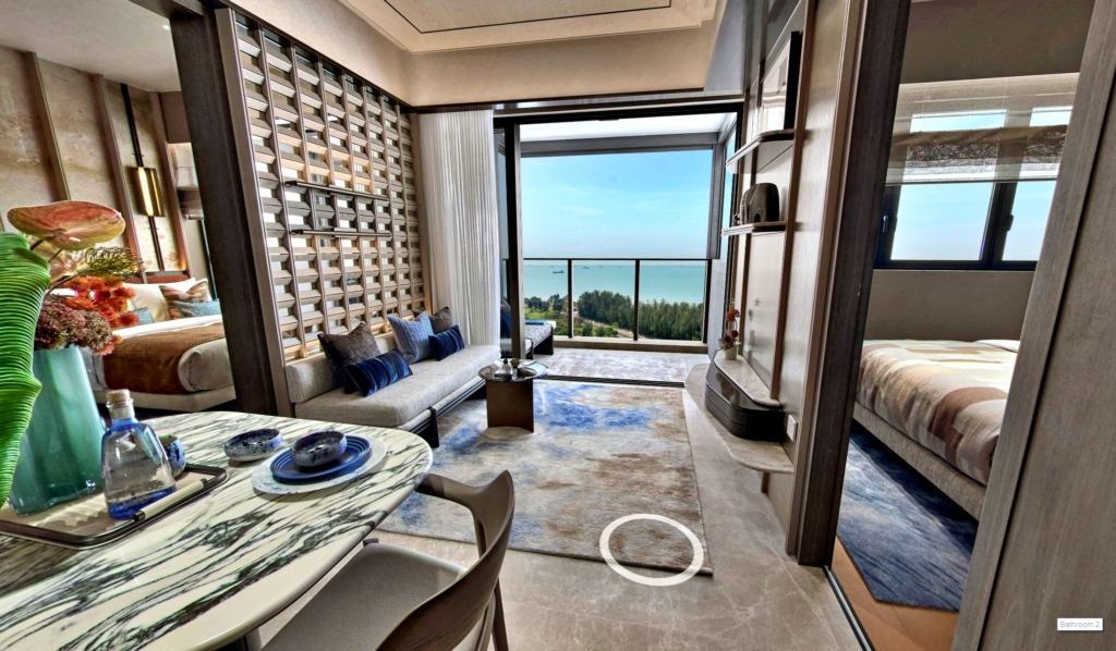 Interior view of a Meyer Blu condo (Tel:+6587865200) 2 bedroom unit living space with a balcony overlooking the sea. The living room features a sofa, rug, and decorative wall panels, while two bedrooms are visible on either side. A dining table with place settings is in the foreground.