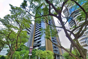 3 Orchard By The Park, A modern high-rise residential building with glass and light-colored facade is partially obscured by lush green trees. Other tall buildings are visible in the background.