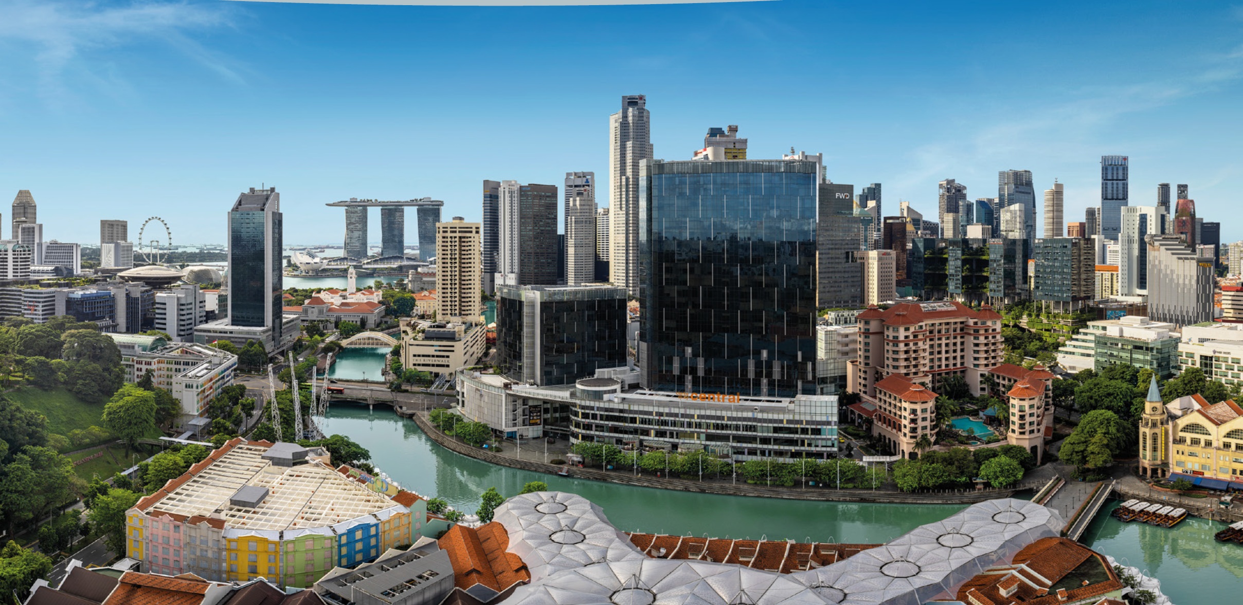 An aerial view of the Singapore River with a dense cityscape featuring modern skyscrapers, historic buildings, and the Marina Bay Sands in the distance.
