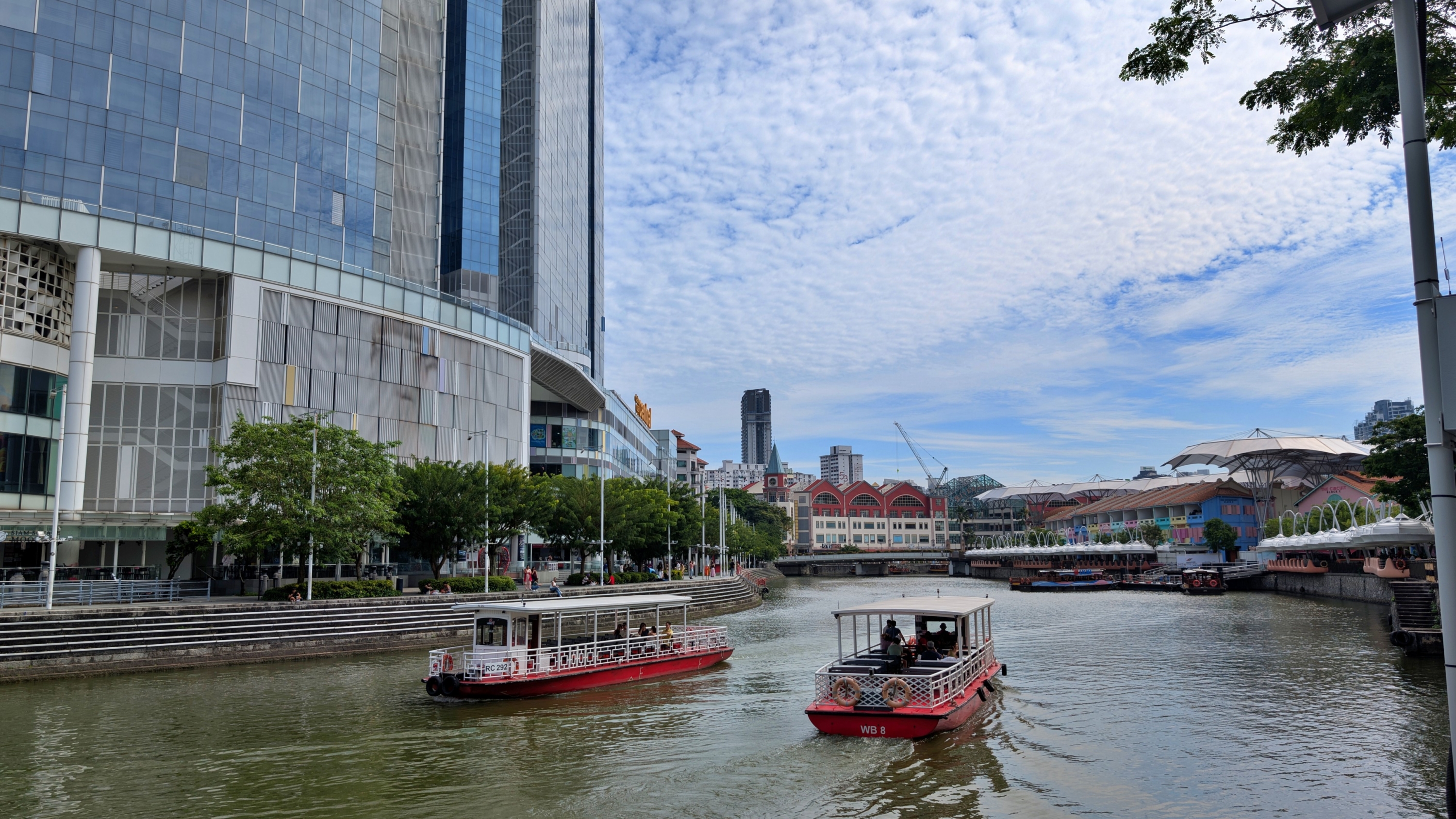A view of the Singapore River with historic shophouses and modern skyscrapers along its banks, and boats on the water.