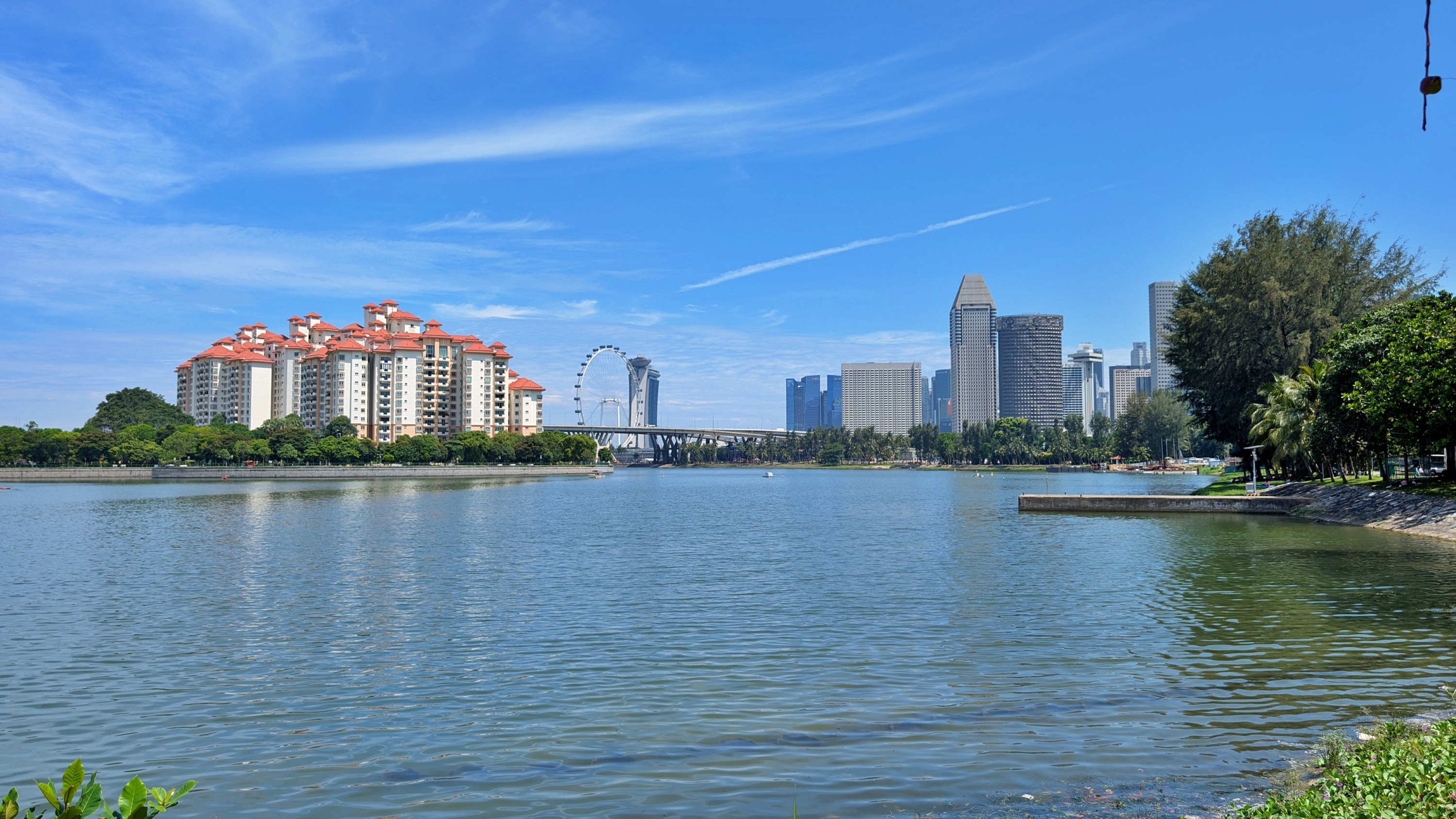 A wide shot of a calm body of water with a city skyline in the background, including a Ferris wheel and residential buildings.